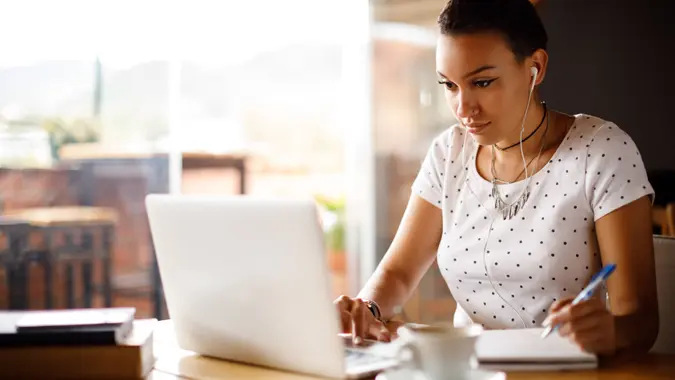 Attractive young woman working on laptop and taking notes at a cafe.