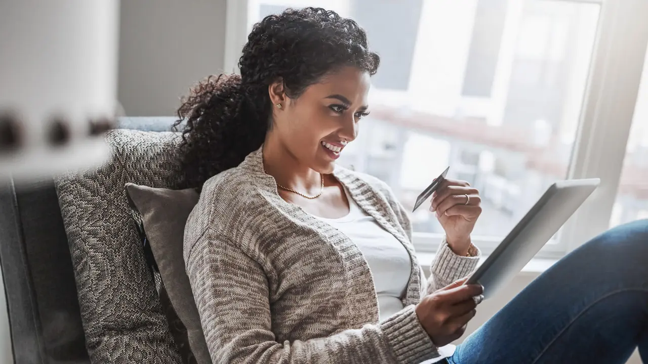 Shot of a cheerful young woman relaxing on a chair while  doing online shopping on a digital tablet at home.