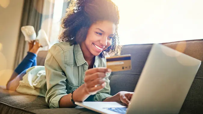 Shot of a cheerful young woman doing online shopping while lying on a couch at home during the day.