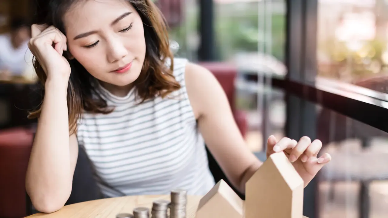 business young woman look at paper house model and coins money stack on wooden table.