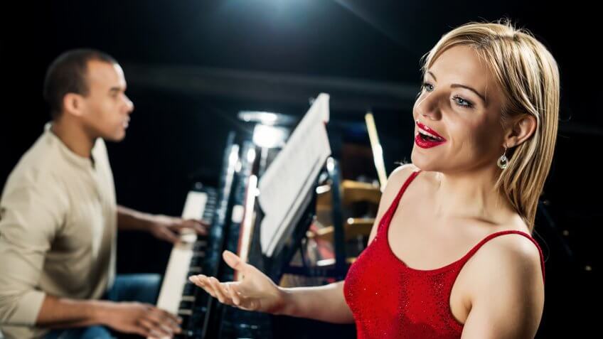 Female opera singer singing, while the pianist is playing the piano in the background.