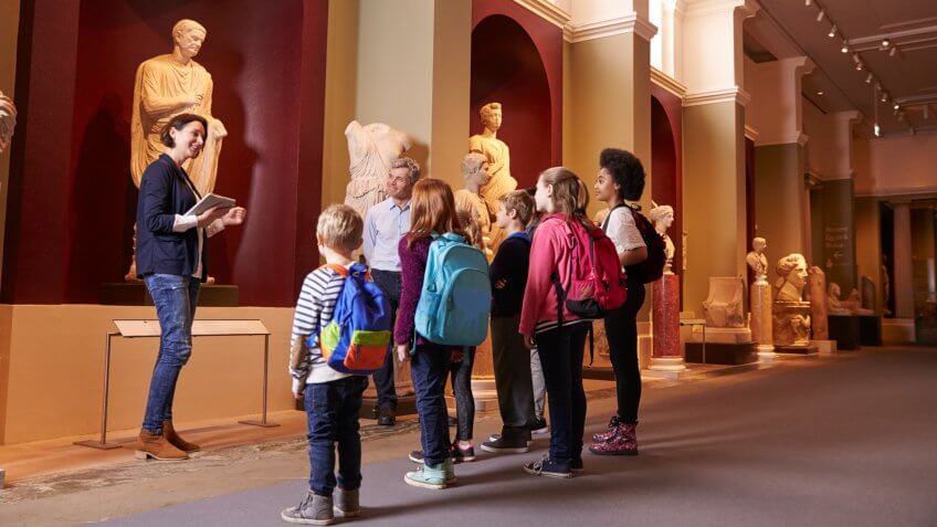 Pupils And Teacher On School Field Trip To Museum With Guide.