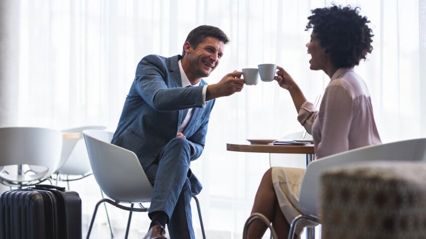 Business partners sitting at airport cafeteria making a toast with coffee cups.