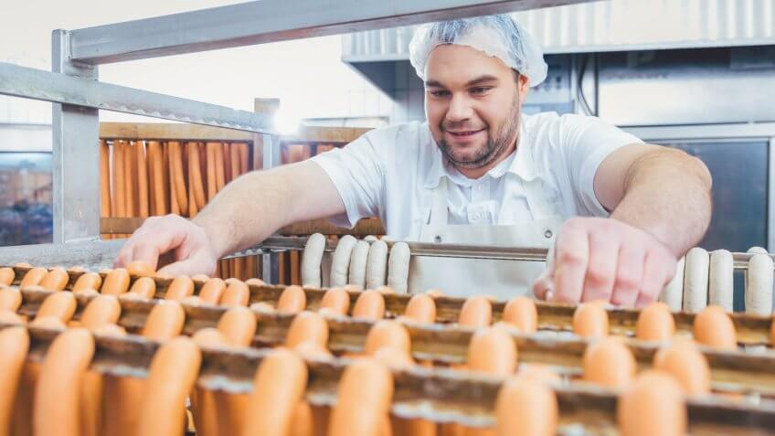 Butcher man making sausages ready to be smoked putting them on rack.