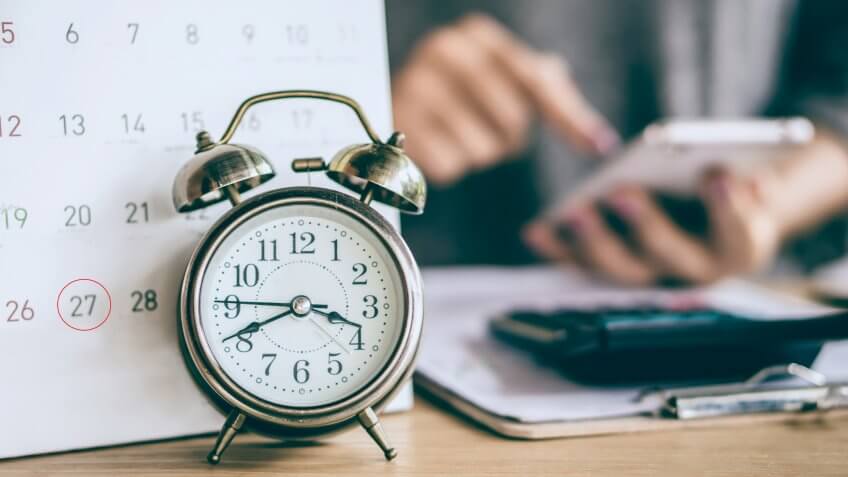 due date calendar and alarm clock with blur business woman hand calculating monthly expenses during tax season.