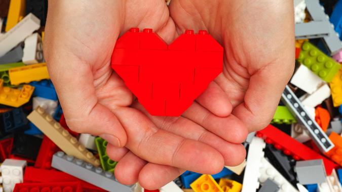 Tambov, Russian Federation - September 07, 2015: Lego red heart in woman hands with Lego blocks background.