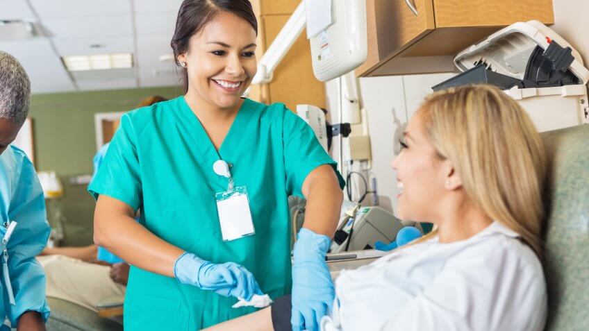 Nurse bandaging arm after patient donates blood in hospital bank.