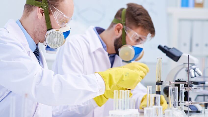 Scientist in protective glasses and masks making experiment in lab.