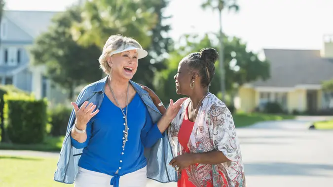 Two multi-racial senior woman, one Caucasian and the other African American, taking a walk in a residential neighborhood on a bright, sunny summer or spring day.
