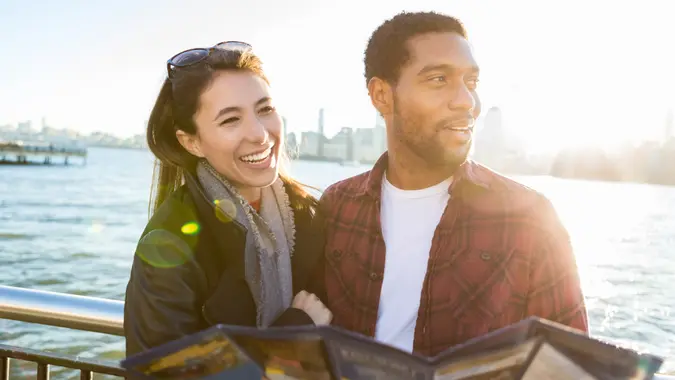 A young couple stands on a city pier in the sunlight.