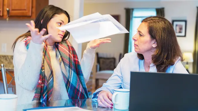 On a breakfast table mother and daughter arguing over increased utility bills and credit card expenses.