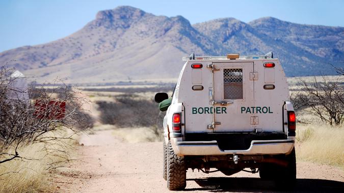 Back of a border patrol truck driving on a dirt road along the Mexican border in Arizona, with mountains in the background.