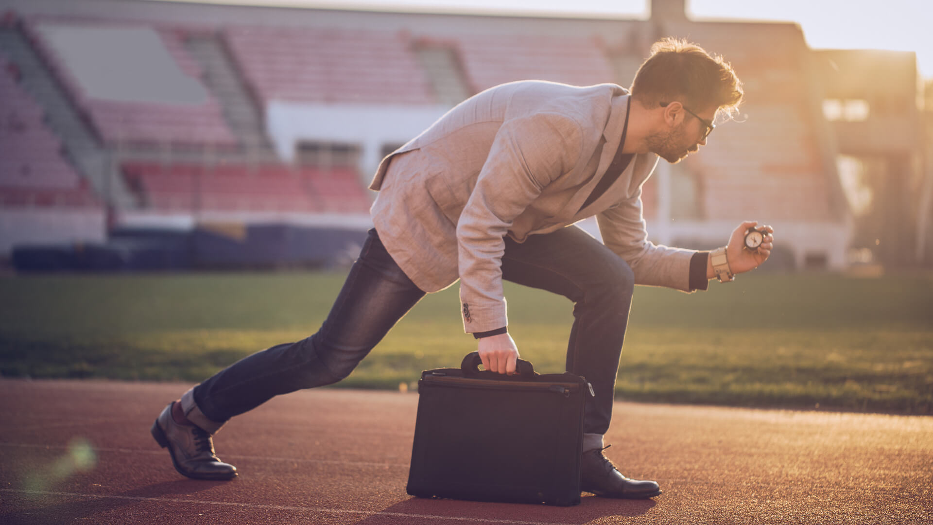 Manager thinking about how to start a business, while leaving starting blocks on the running track and holding briefcase and stopwatch.
