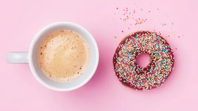 Morning coffee cup and sweet pastry of chocolate donut on pink pastel table top view.
