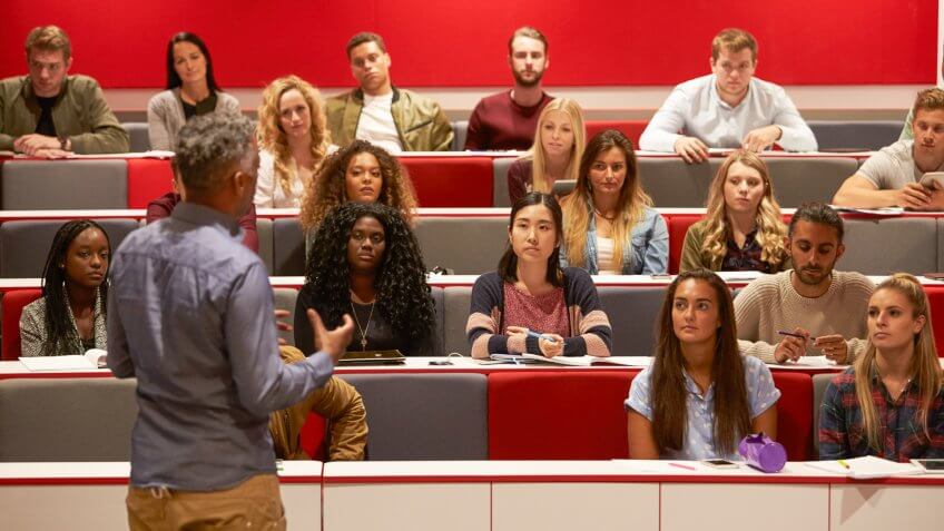 Back view of man presenting to students at a lecture theatre.