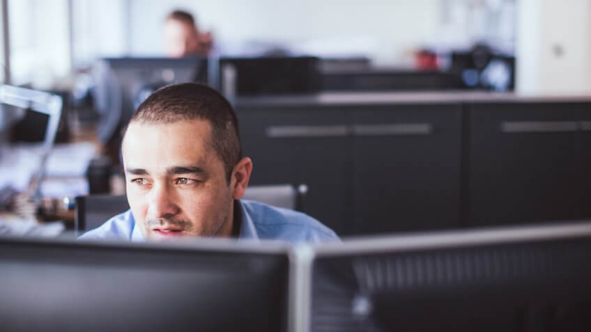 A photo of businessman looking away while sitting at computer desk.