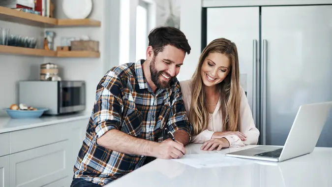 Shot of a young couple using a laptop and going through paperwork at home.