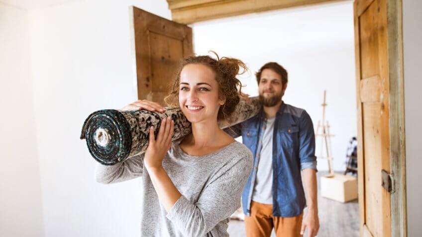 Young couple moving in new house, carrying a carpet.