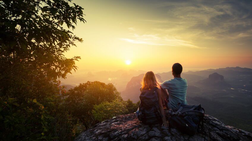 Two hikers on top of the mountain enjoying sunrise over the tropical valley.