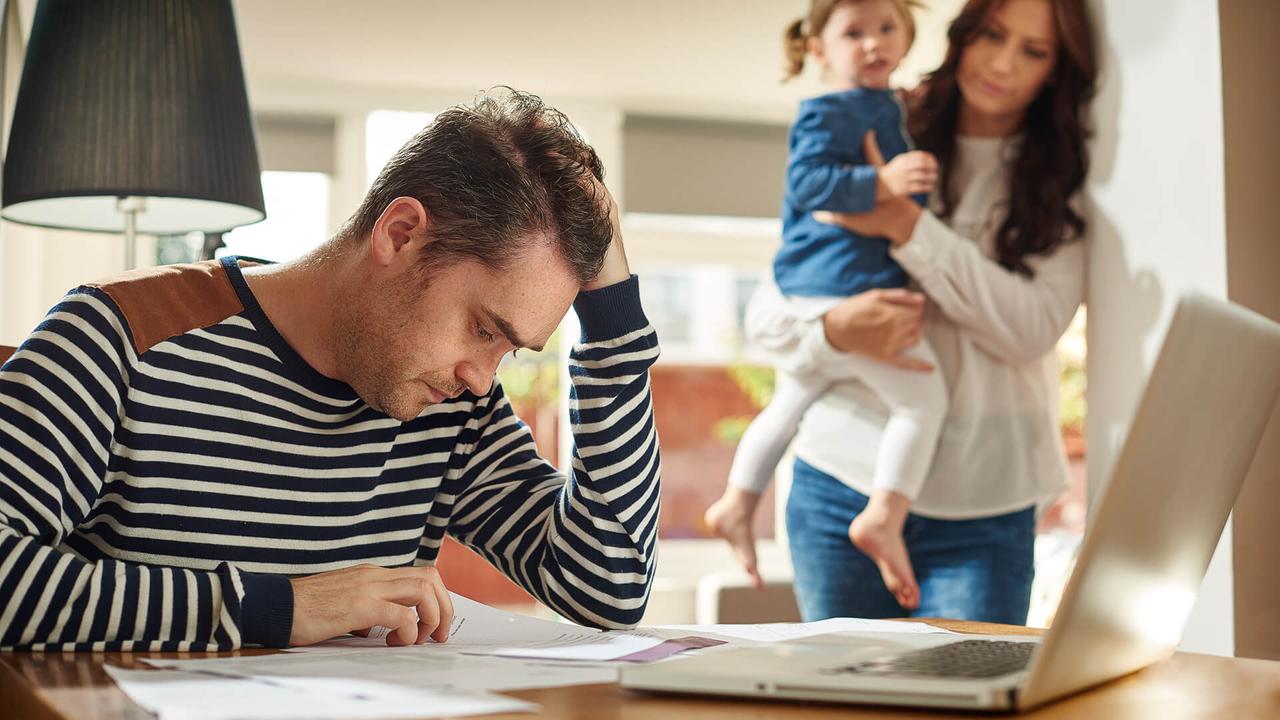 A young husband and father sits at a dining table looking through the household bills and holds his head in despair .