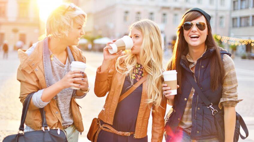 Young friends together walking in the city, talking and drinking coffee from paper cup.