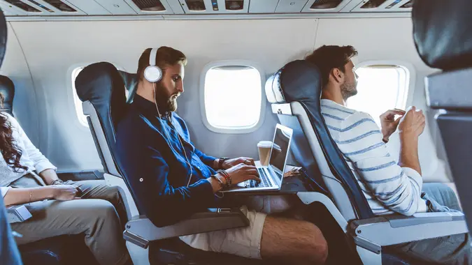 Young bearded man sitting inside an airplane and using a laptop.