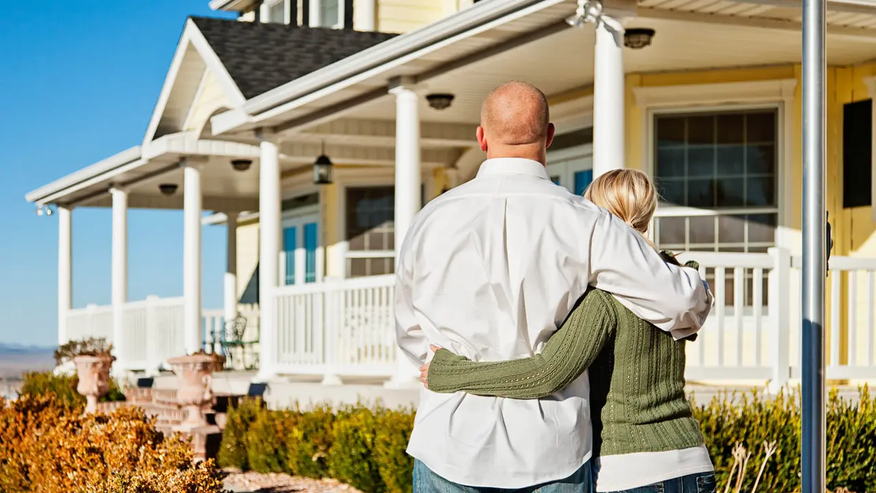 Photo of young couple standing in front of their new home, standing close together as they admire it.