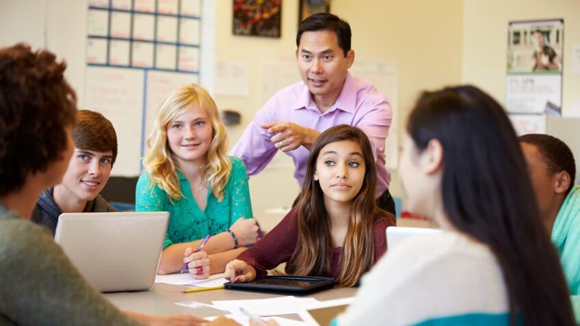 High School Students With Teacher In Class Using Laptops Smiling.