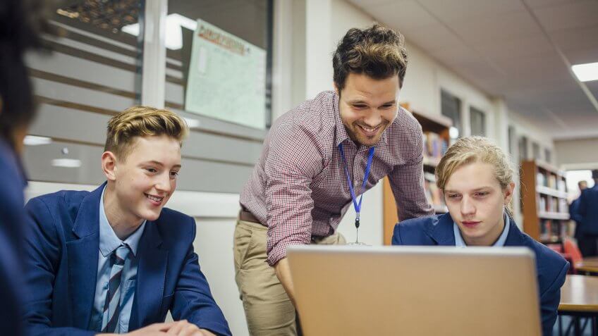 male high school teacher with students on laptop