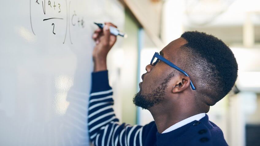 Cropped shot of a young man writing on a whiteboard in a classroom.