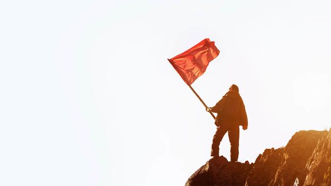 man holding red flag at mountain top