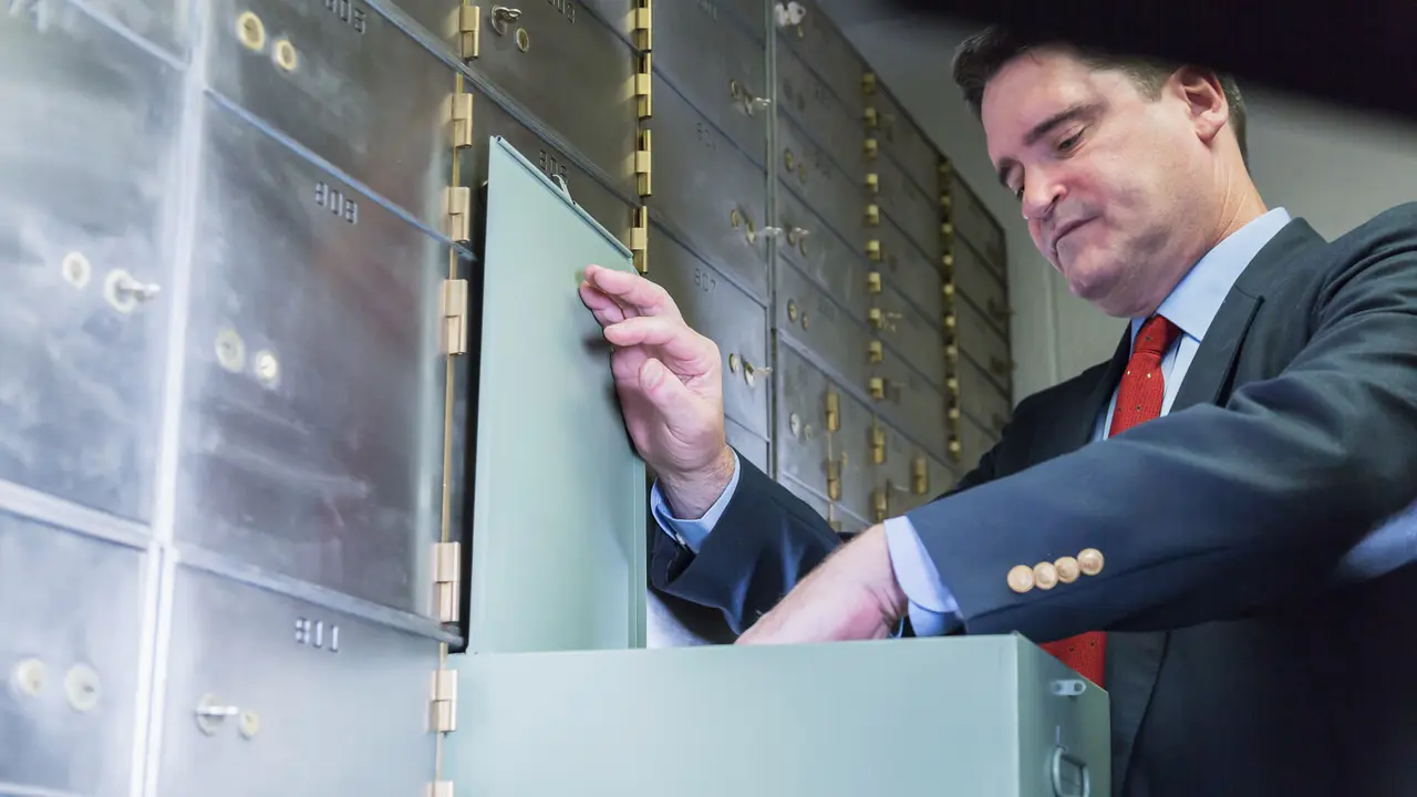Mature man wearing a business suit opening a safety deposit box, looking inside.
