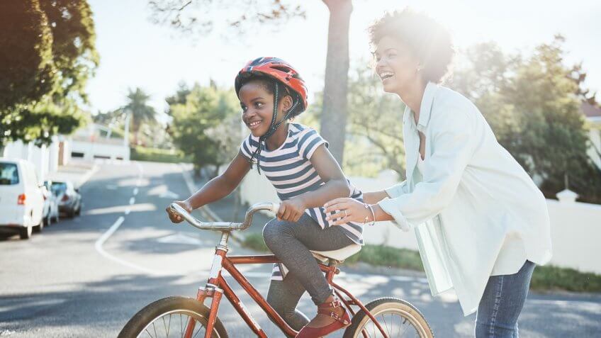 cheerful young father helping his son to ride his bike outside during the day.