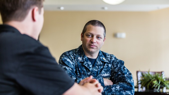 A 15 year old civilian male teenager is sitting with a United States Navy Officer recruiter.
