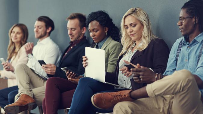 Shot of a group of businesspeople using different wireless devices while waiting in line for an interview.