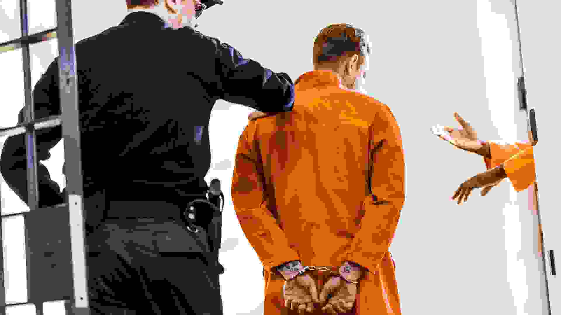 back view of prison guard leading criminal in handcuffs.