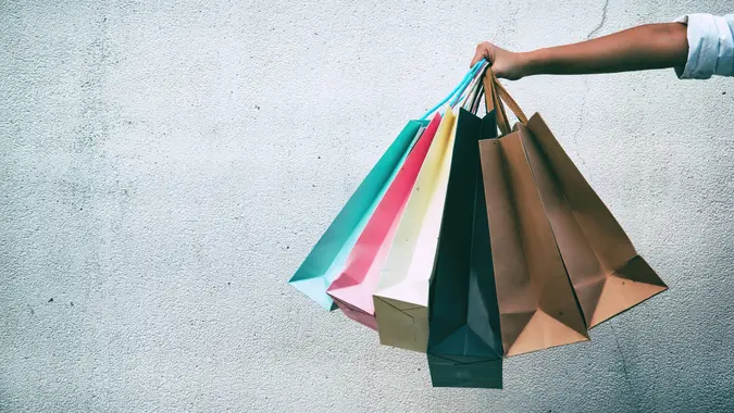 Closeup the colorful shopping bags were holding by lady hand,in front of grunge surface cement wall,in abstract art design,classic old film tone,blurry light around.