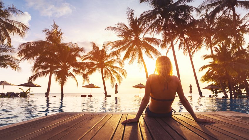 Woman enjoying vacation holidays at luxurious beachfront hotel resort with swimming pool and tropical lansdcape near the beach.