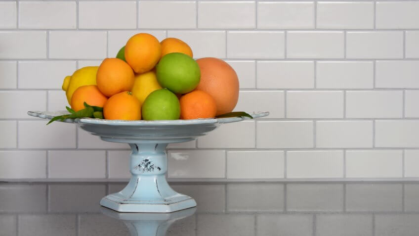 Homegrown selection of citrus fruit in retro modern kitchen with white ceramic subway tile backsplash and quartz countertop.