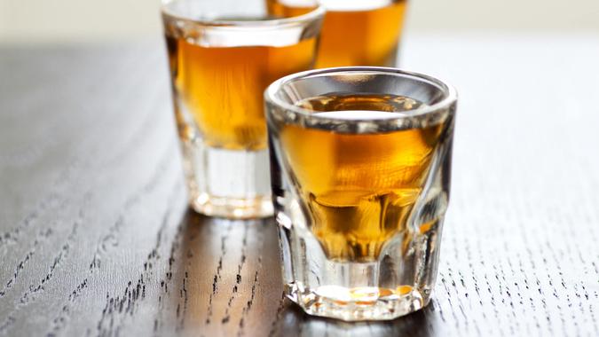 Three shot glasses full of dark colored alcohol on top of a bar table.