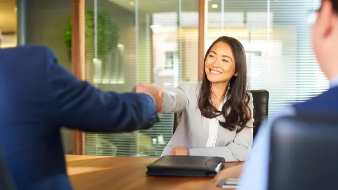 a young woman sits opposite the recruitment manager and shakes his hand as she gets the job.