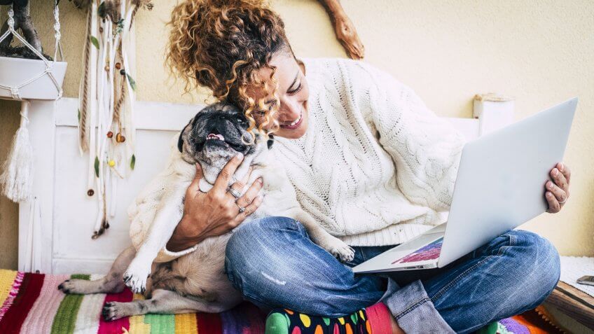 real best friends cheerful woman working at laptop on the terrace at home while hug her best love and friends smiling dog pug sitting at his left.