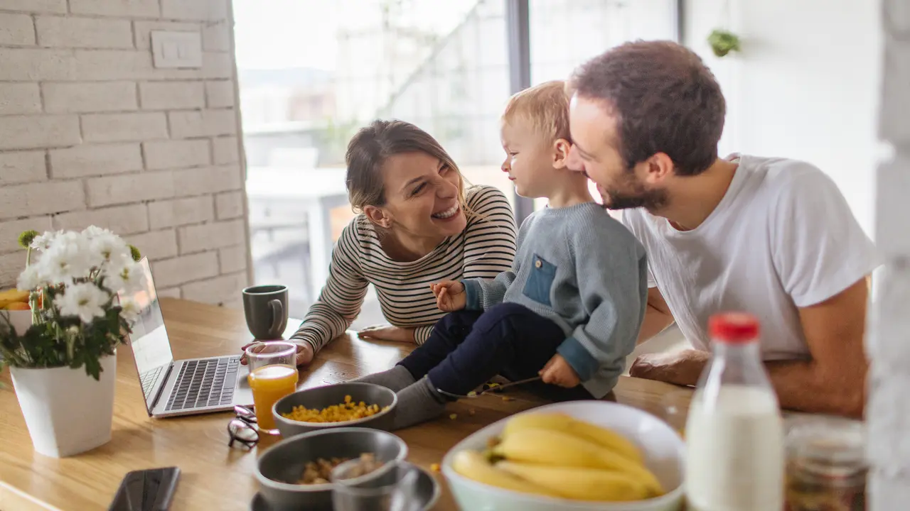 Photo of a young family using computer during meal time - so their toddler boy can stay calm and focused while sitting at the table.