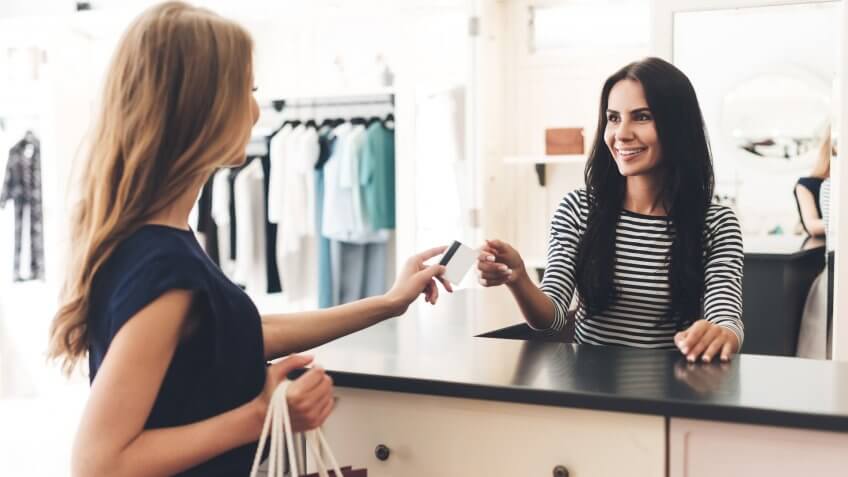 Can I pay with my card? Young woman with shopping bags giving her credit card to seller while standing at the clothing store.