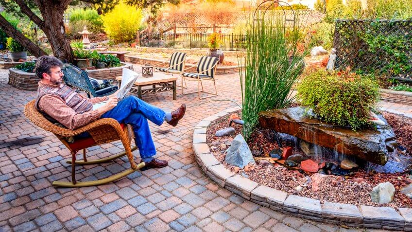 Man is reading a newspaper on a patio in a cozy garden.
