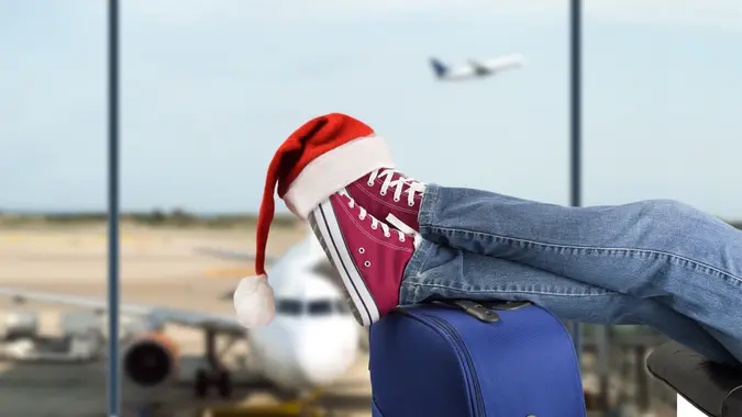 young boy with his legs over the suitcase waiting at the airport with santa hat on the feet.