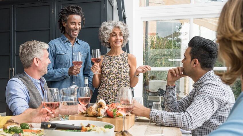 Group of friends having dinner party listening to man and woman holding rose wine.