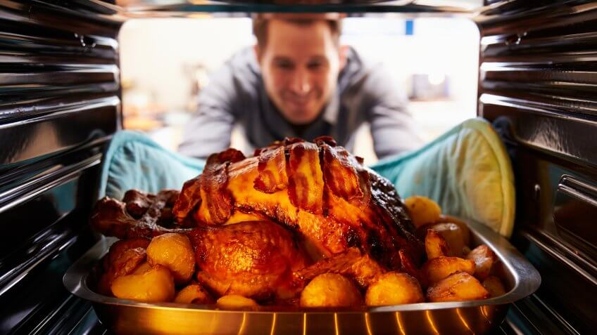 Man Taking Roast Turkey Out Of The Oven.