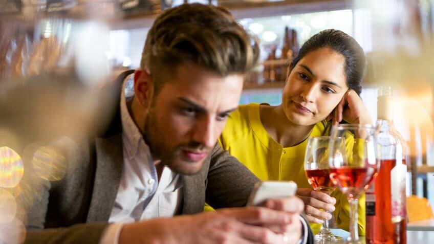 A couple are out having drinks and the woman looks irritated that her partner is on his mobile phone and not paying her any attention.