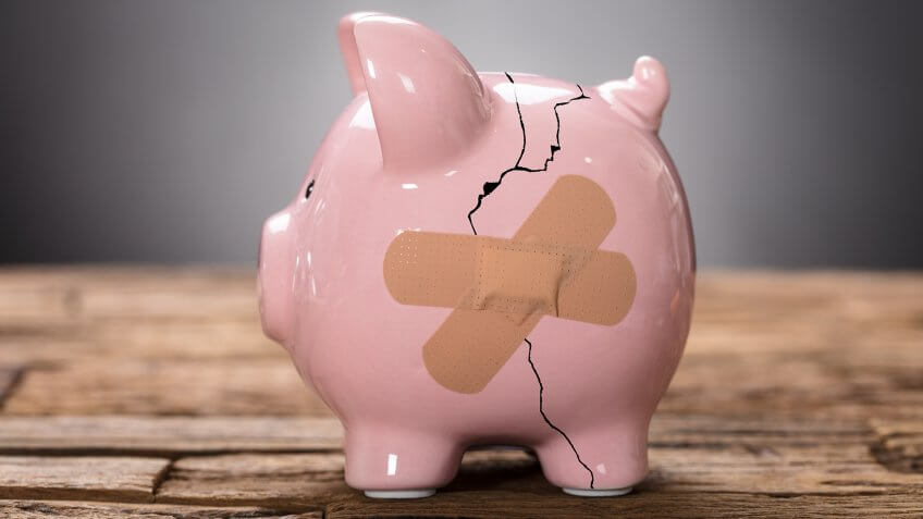 Closeup of broken pink piggybank with bandage on wood.